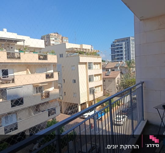 מרפסת עם רשת נגד יונים ונוף עירוני